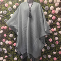 Gray poncho with fringe on a mannequin against a floral wall.