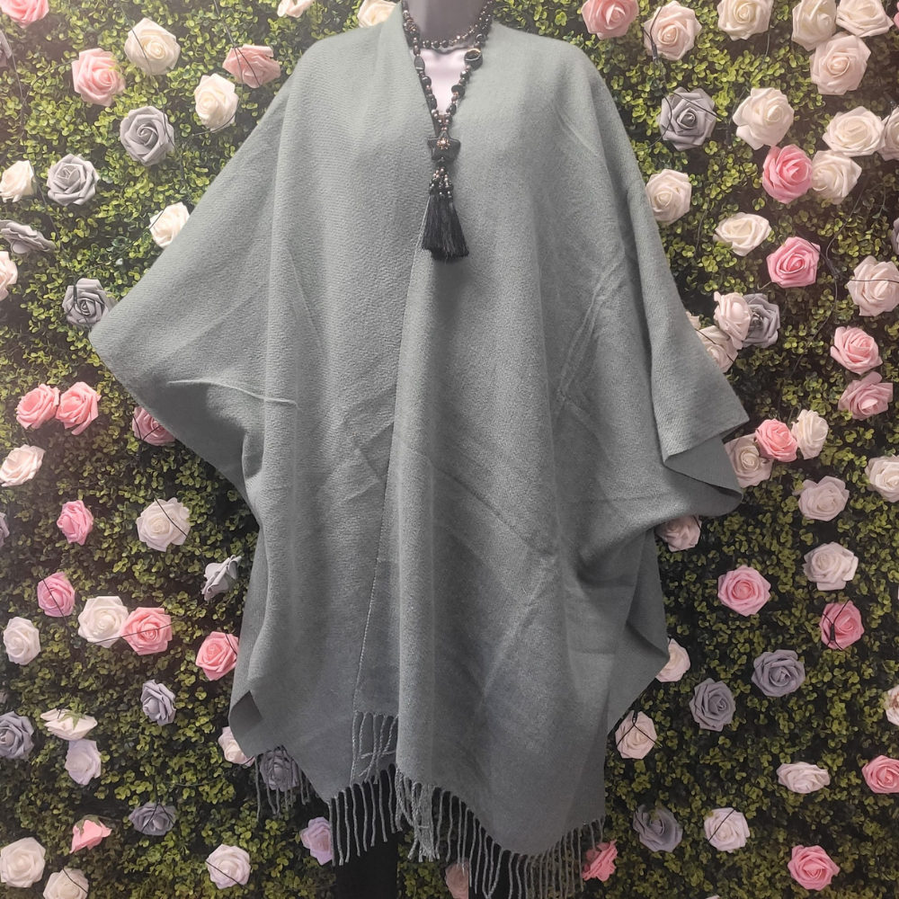 Gray poncho with fringe on a mannequin against a floral wall.