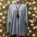 Mannequin wearing a light blue jumper with a long necklace against a floral wall.