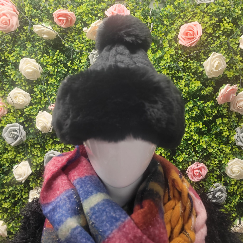 Black Bobble Hat with a fur trim on a mannequin in front of a greenery and floral wall.