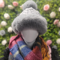 Grey Wool and Faux Gur Bobble hat on a mannequin in front of a floral and greenery wall