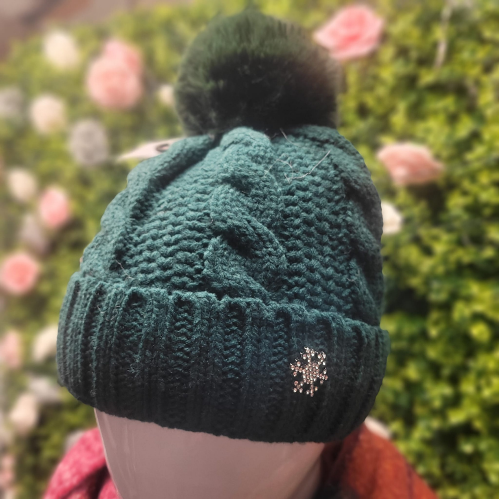 Green knitted beanie with a pom-pom on a mannequin head against a blurred floral background