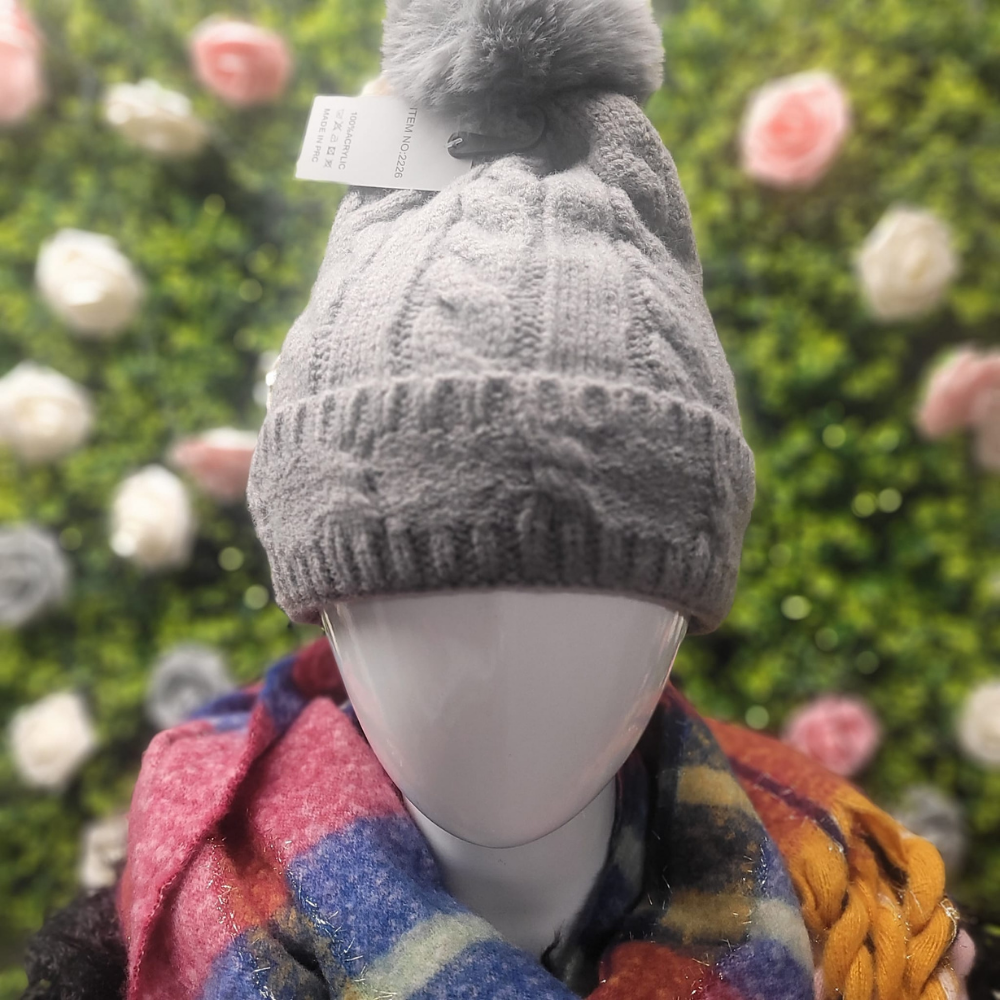 Gray knit beanie on a mannequin with a colorful scarf against a floral background