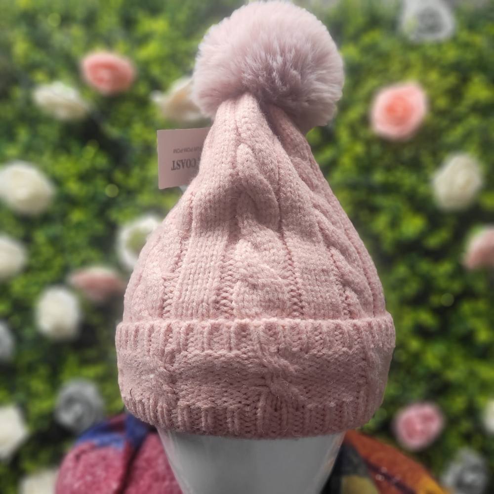 Pink knit beanie with a pom-pom on a mannequin head against a floral background