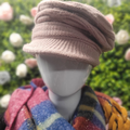 Mannequin wearing a dusky pink knitted hat with a blurred floral background