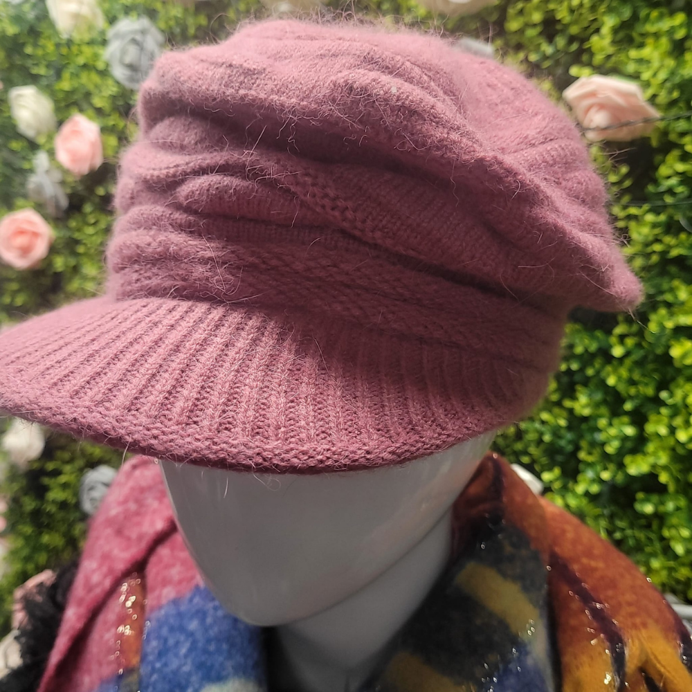 Mannequin wearing a pink knitted hat with a colorful scarf against a blurred floral and greenery background