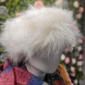 Close-up of a mannequin head with a fluffy white hairpiece against a blurred floral background.