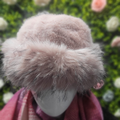 Mannequin head wearing a pink fur hat with a blurred floral background