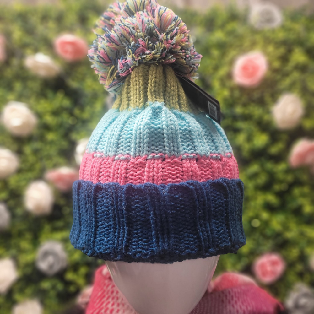 Colorful striped knit hat with a pom-pom on a mannequin against a blurred floral background