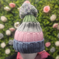 Knitted hat with gradient colors held against a blurred floral background