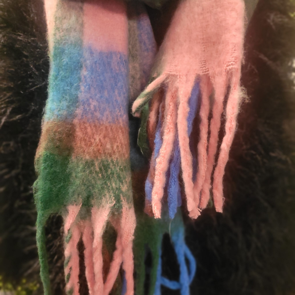 Multicolored scarf with fringes held by a person against a dark background