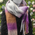 Multicolored scarf with purple, orange, and gray hues on a mannequin against a blurred floral background.