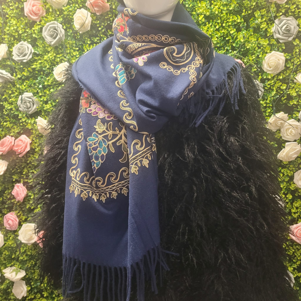 Blue embroidered scarf with gold patterns on a black feathered garment against a floral and green leafy background.