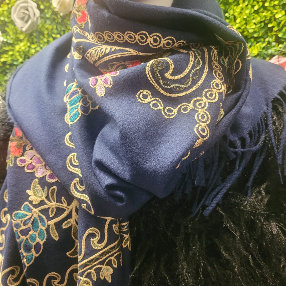 Navy blue scarf with gold paisley patterns worn over a dark coat against a blurred green background