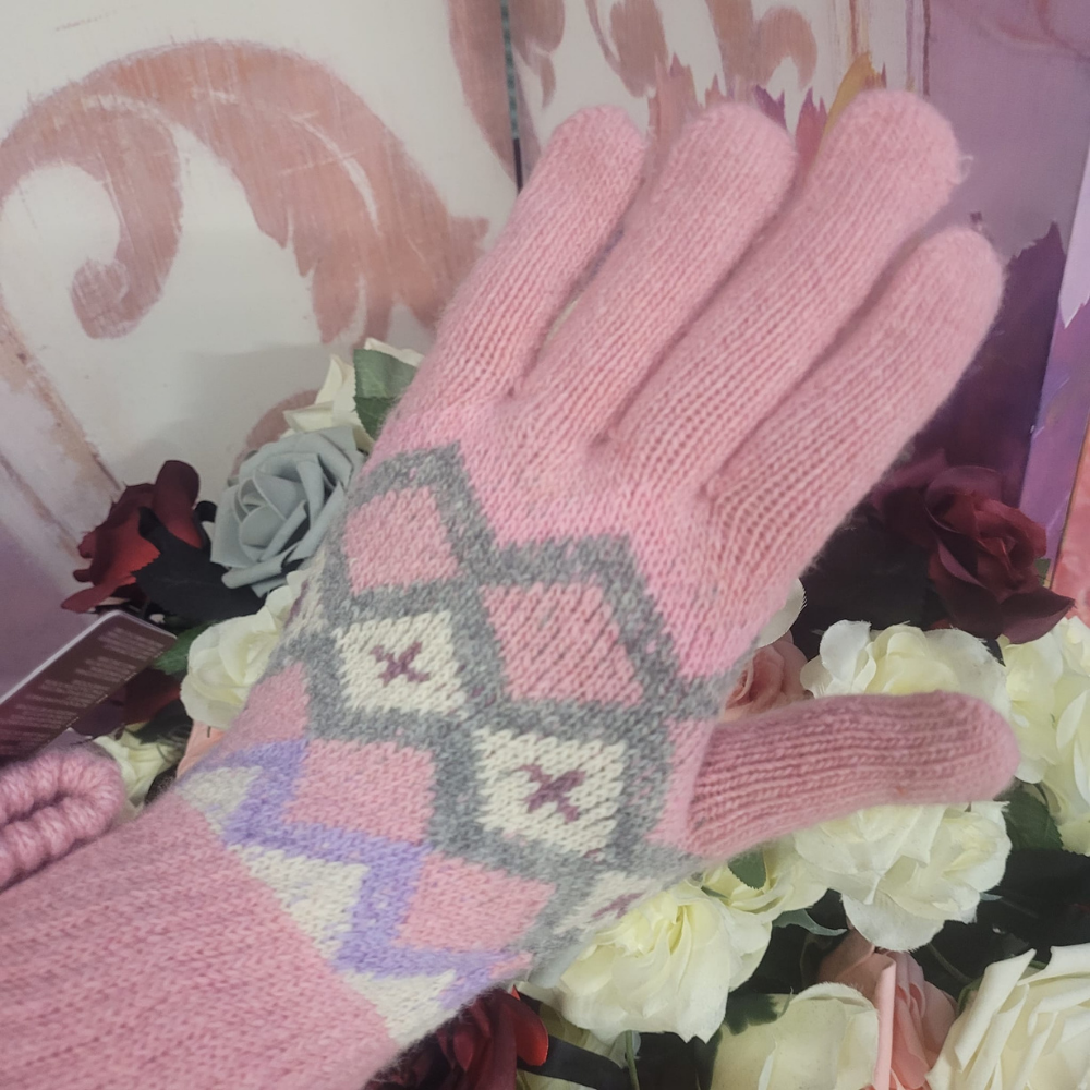 Pink knitted gloves with a geometric pattern held over flowers and a heart-shaped object.