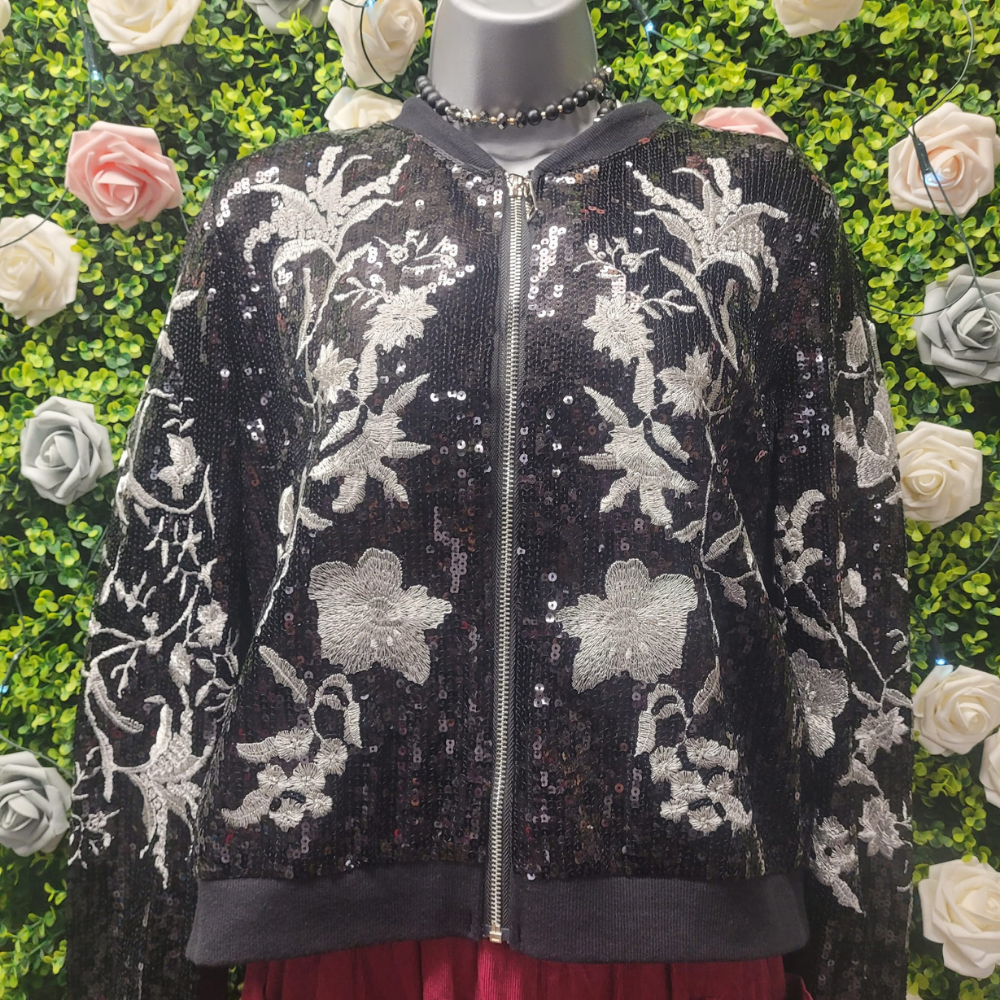 Black sequin jacket with floral patterns on a mannequin against a green foliage and rose background
