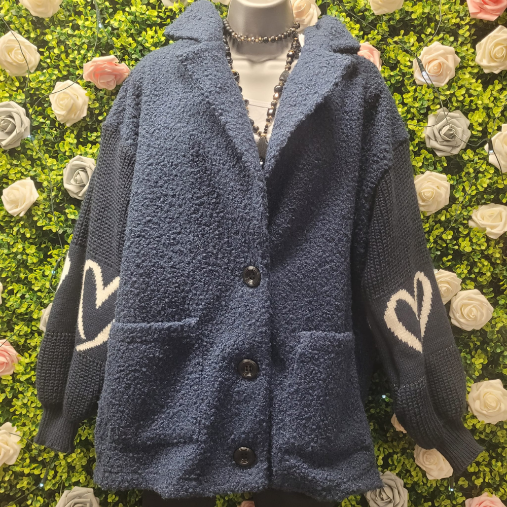 Blue textured cardigan with heart designs on a mannequin against a floral background