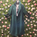 Green coat displayed on a mannequin against a floral wall.