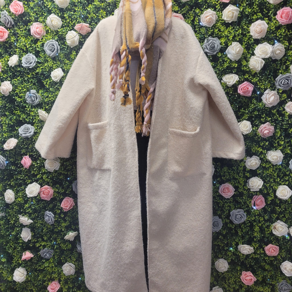 Ivory longline jacket on a mannequin on a backdrop of greenery.