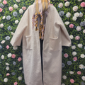 Ivory longline jacket on a mannequin on a backdrop of greenery.