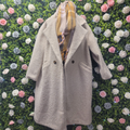 Biscuit jacket on a mannequin on a backdrop of greenery wall.