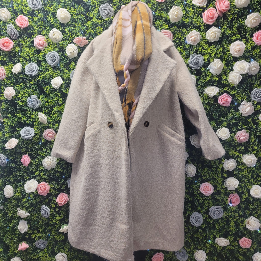 Biscuit jacket on a mannequin on a backdrop of greenery wall.