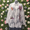 White lace shirt with embroidered designs on a mannequin against a floral background