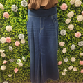 Person wearing blue jeans standing against a green wall with floral decorations