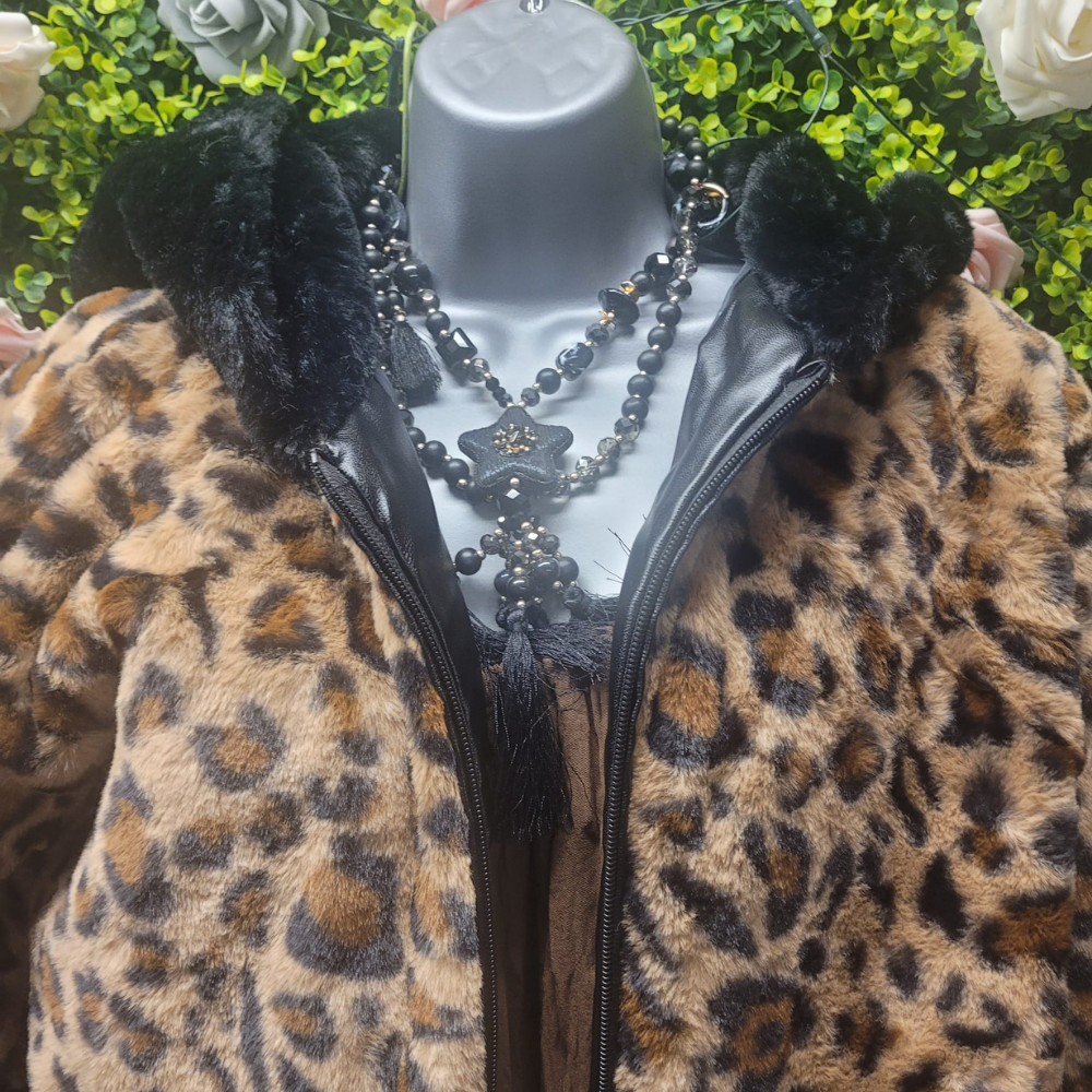 Leopard print coat with black fur trim on a mannequin against a green leafy background